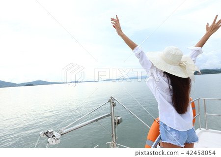 Asian Mix Race Tanned skin Woman Bikini White Shirt Big Hat short jean stand on deck of Yacht Boat with orange life buoy under summer blue sky in vacation holiday, copy space text logo Asian Mix Race Tanned skin Woman Bikini White Shirt Big Hat short jean stand on deck of Yacht Boat with orange life buoy under summer blue sky in vacation holiday, copy space text logo 42458054