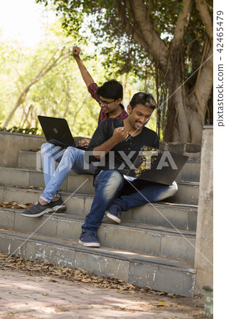 Happy young students working on laptop in park Happy young students working on laptop in park 42465479