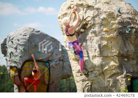 Photo of sports men and women climbing on boulders for rock climbing against blue sky with clouds 42469178