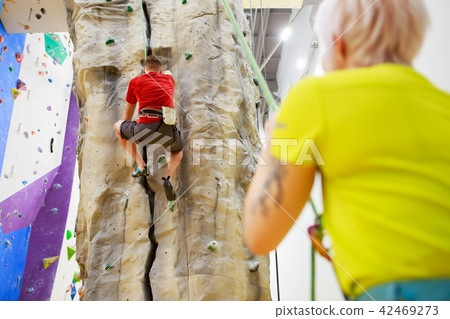 Photo of sporty man on climbing wall and female trainer Photo of sporty man on climbing wall and female trainer 42469273