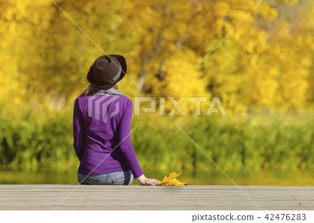 Girl in a hat sits on the dock and admires colors Girl in a hat sits on the dock and admires colors 42476283