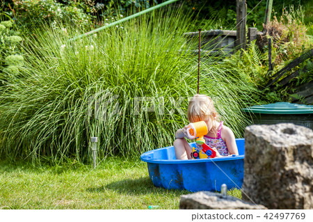 Little girl enjoying a hot summer day while usin her sandpit as swimming pool Little girl enjoying a hot summer day while usin her sandpit as swimming pool 42497769