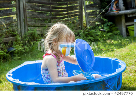 Little girl enjoying a hot summer day while usin her sandpit as swimming pool 42497770