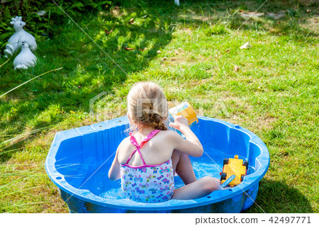 Little girl enjoying a hot summer day while usin her sandpit as swimming pool Little girl enjoying a hot summer day while usin her sandpit as swimming pool 42497771