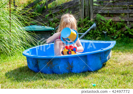 Little girl enjoying a hot summer day while usin her sandpit as swimming pool Little girl enjoying a hot summer day while usin her sandpit as swimming pool 42497772