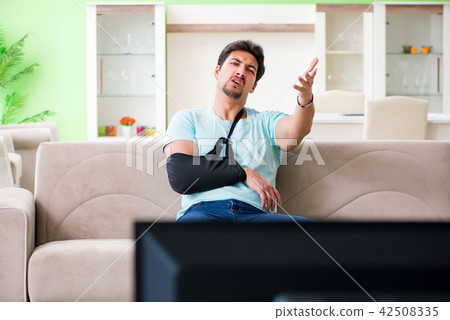 Arm injured man sitting on the sofa watching tv Arm injured man sitting on the sofa watching tv 42508335