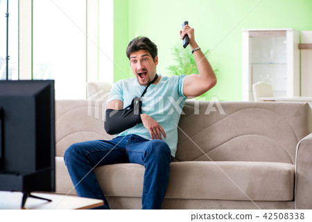 Arm injured man sitting on the sofa watching tv Arm injured man sitting on the sofa watching tv 42508338