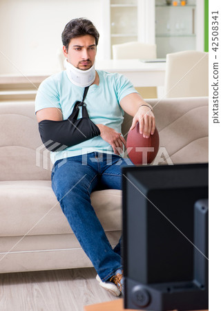 Man with neck and arm injury watching american football on tv Man with neck and arm injury watching american football on tv 42508341