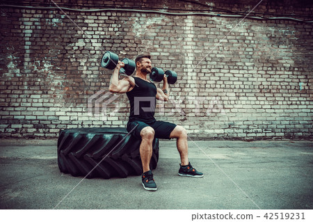 Muscular guy doing exercises with dumbbell against a brick wall 42519231