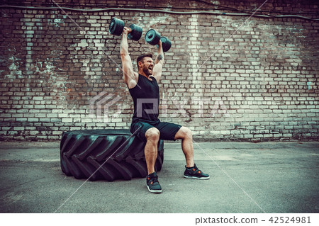 Muscular guy doing exercises with dumbbell against a brick wall Muscular guy doing exercises with dumbbell against a brick wall 42524981