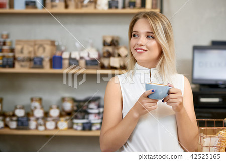 Pretty girl drinking coffee in shop, looking at side. Pretty girl drinking coffee in shop, looking at side. 42525165
