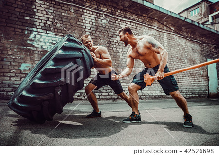 Two muscular athletes training. Muscular fitness shirtless man moving large tire 42526698