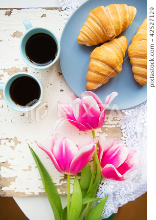 coffee, croissants and three beautiful pink tulips on old white table coffee, croissants and three beautiful pink tulips on old white table 42527129