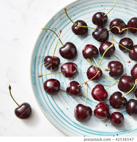 Ripe sweet cherry in the blue plate on a gray stone background. Top view. Ripe sweet cherry in the blue plate on a gray stone background. Top view. 42536547