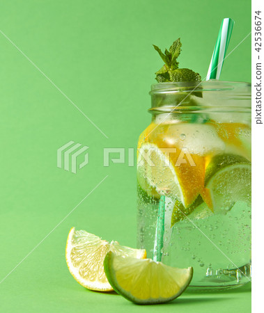 Fresh cold homemade cocktail on a green background. Citrus fruits slices of lemon and lime, ice Fresh cold homemade cocktail on a green background. Citrus fruits slices of lemon and lime, ice 42536674