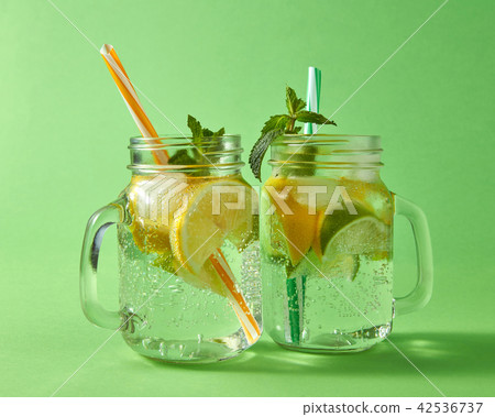 Citrus fruits slices of lemon and lime, ice, water and plastic straws in the glass on a green Citrus fruits slices of lemon and lime, ice, water and plastic straws in the glass on a green 42536737