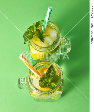 Citrus fruits slices of lemon and lime, ice, water and plastic straws in the glass on a green Citrus fruits slices of lemon and lime, ice, water and plastic straws in the glass on a green 42536779