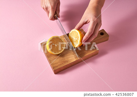 Slices of yellow lemon on a wooden board on a green. Female hands cutting a ripe lemon for preparing 42536807