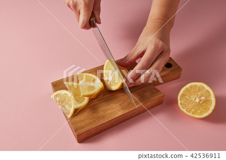 Citrus fruit natural lemon on cutting board. Female hands cutting a yellow ripe lemon on half on a 42536911