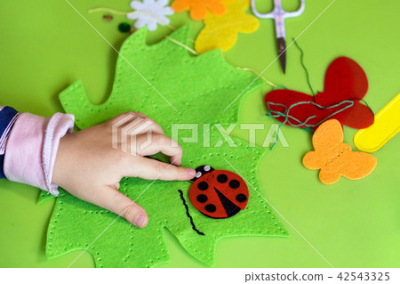 Child making felt soft toy of green leaf and red ladybag . Child DIY activity. Close-up. Children 42543325