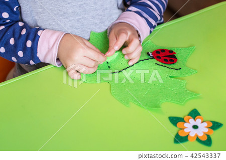 Child making felt soft toy of green leaf and red ladybag . Child DIY activity. Close-up. Children Child making felt soft toy of green leaf and red ladybag . Child DIY activity. Close-up. Children 42543337