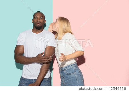 The young couple whispering a secret behind her hand over studio background 42544336
