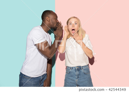 The young couple whispering a secret behind her hand over studio background 42544349