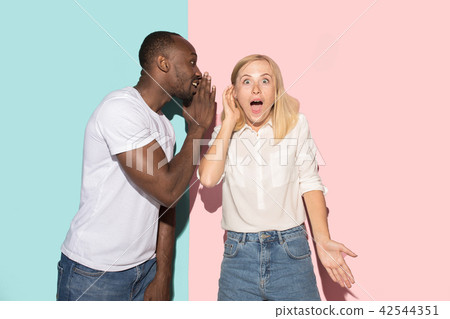 The young couple whispering a secret behind her hand over studio background 42544351