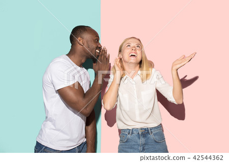 The young couple whispering a secret behind her hand over studio background The young couple whispering a secret behind her hand over studio background 42544362