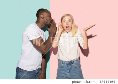 The young couple whispering a secret behind her hand over studio background The young couple whispering a secret behind her hand over studio background 42544365