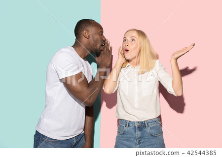 The young couple whispering a secret behind her hand over studio background The young couple whispering a secret behind her hand over studio background 42544385