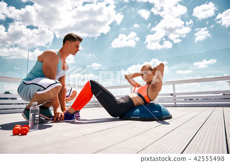 Concentrated woman is having workout with man on balcony Concentrated woman is having workout with man on balcony 42555498