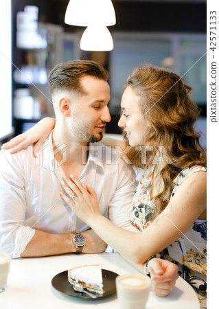 Young couple sitting at cafe with cups of coffe, cake and hugging. 42571133