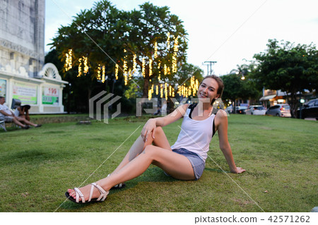 Young woman sitting on lawn, wearing shirt and shorts. Young woman sitting on lawn, wearing shirt and shorts. 42571262