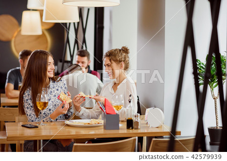 Positive female friends chatting and eating in pizzeria. Positive female friends chatting and eating in pizzeria. 42579939