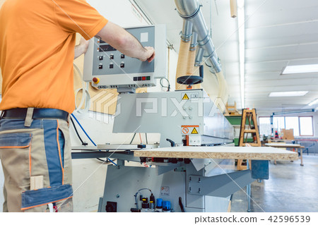 Carpenter in furniture factory pressing button on machine 42596539