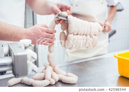 Worker working in butchery producing sausages putting them on beam 42596544