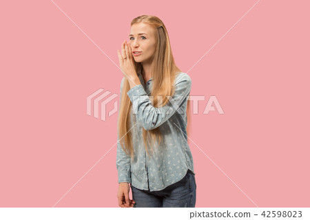 The young woman whispering a secret behind her hand over pink background 42598023