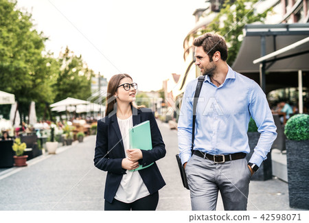 A young businessman and businesswoman walking on a sidewalk. 42598071