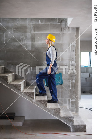 Woman worker with a tool box walking up the stairs on the construction site. 42598099