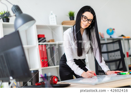 A young girl stands near a computer desk and draws a marker on a magnetic board. 42602416
