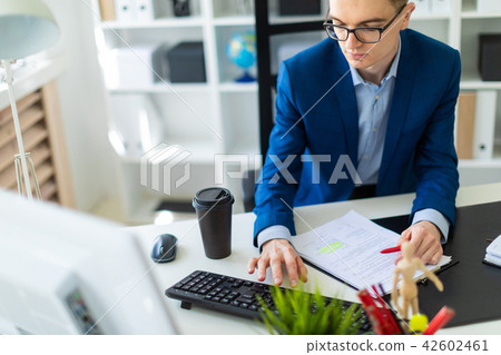 A young man sits at a table in the office and works with documents and a computer. A young man sits at a table in the office and works with documents and a computer. 42602461