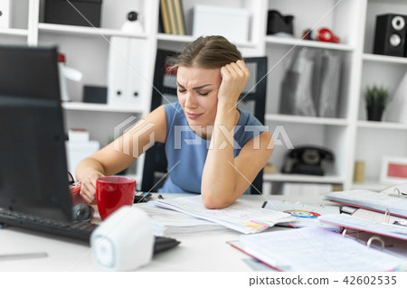 A young girl sits in the office at a computer desk and propps her hand on her head. A young girl sits in the office at a computer desk and propps her hand on her head. 42602535
