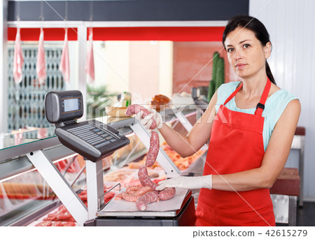 Female seller weighing sausages in shop Female seller weighing sausages in shop 42615279