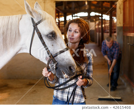 Woman farmer standing with white horse, man cleaning floor 42615408