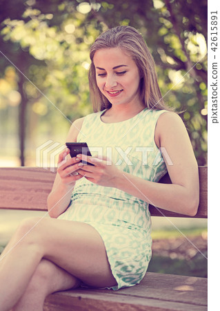girl sitting on a bench and using phone in park 42615891