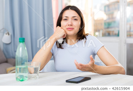 Upset girl suffering from troubles at table with bottled water Upset girl suffering from troubles at table with bottled water 42615904