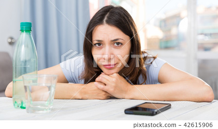 Upset girl suffering from troubles at table with bottled water Upset girl suffering from troubles at table with bottled water 42615906