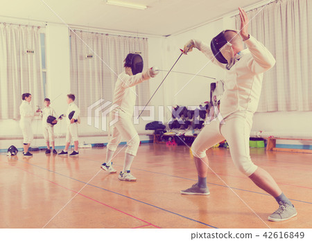 Adults and teens wearing fencing uniform practicing with foil Adults and teens wearing fencing uniform practicing with foil 42616849