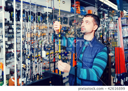 thoughtful male choosing fishing rod for fishing in the sports shop 42616899